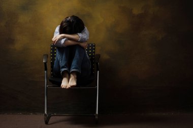 Sandalyede otururken yüzünü kaşıyan maskeli bir kadın. COVID-19 ile ilgili depresyon.