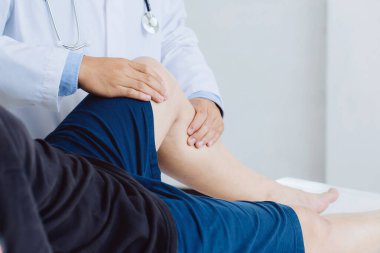 Erkek hastanın yaralı bacağını tedavi eden ve fizyoterapi kliniğindeki erkek hastaya egzersiz yaptıran fizyoterapist doktor. .