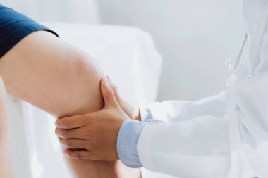 Doktor fizyoterapist yaralı dizini tedavi ediyor, sapını hastanın dizine dayayıp ağrısını kontrol ediyor..
