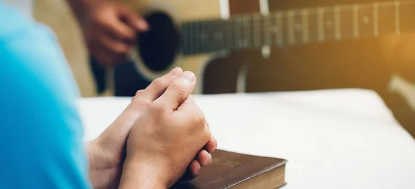Homem Rezando Sobre Bíblia Sagrada Mesa Madeira Amigos Tocando Guitarra — Fotografia de Stock