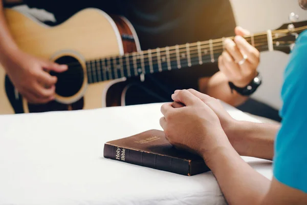 Man praying  over holy bible on wooden table And friends playing guitar with the light from above with copy space for your text