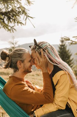 Parlak elbiseli güzel bir çift dağların arasında bir hamakta yatıyor. Gerçek duygular, aşk ve mutluluk..