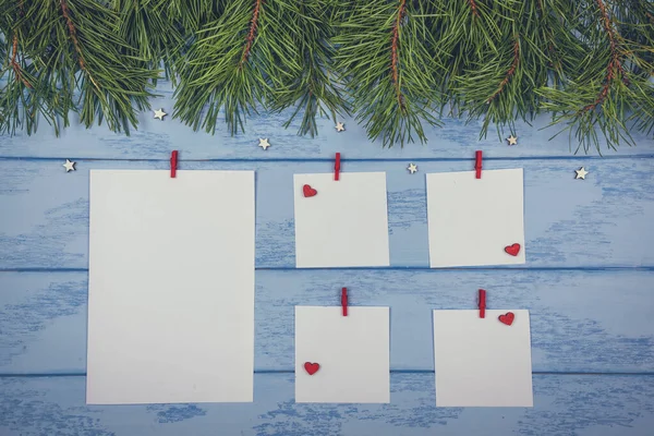 Christmas or New Year mock up: pine branches and white stickers with red clothespins, little wooden stars and hearts on the blue boards.