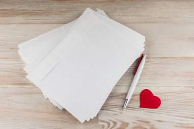 love mail: the pack empty blank white envelopes for letters, white ball-point pen and a red heart lies on a light wooden table next to the right