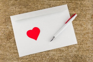 Aşk mektubu: mektuplar için beyaz boş zarf, beyaz top kalem ve kırmızı kalp keten kumaşın üzerinde duruyor