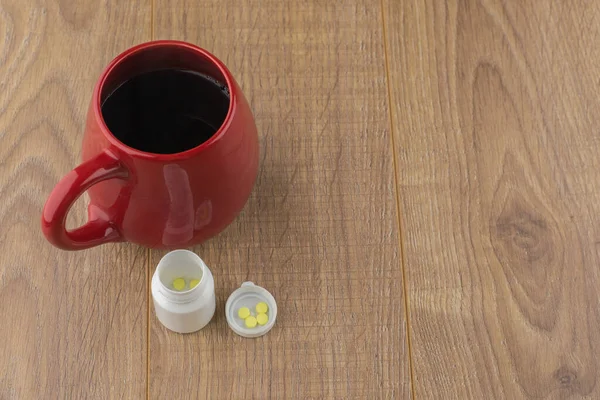 眠気との闘い 錠剤箱の近くのカフェイン錠剤と木製のテーブルの上の強いコーヒーの赤いカップ — ストック写真