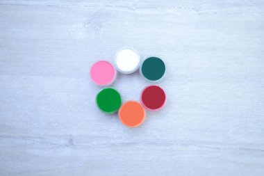 Boyalı çok renkli kavanozlar, beyaz ahşap arka planda guaj.