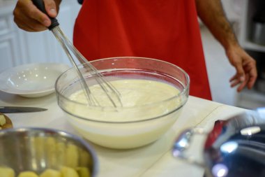 Mutfakta beyaz hamuru kasede karıştıran bir adam var.