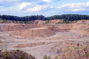 Kenarlarında yeşil ağaçlar olan sarı ve beyaz kumlu derin bir kum çukuru.
