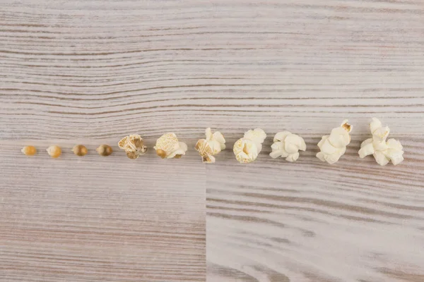 家庭で電子レンジで調理されたポップコーン 列の白いテーブルの上に置かれたトウモロコシのカーネルの準備のさまざまな段階 トップビュー — ストック写真