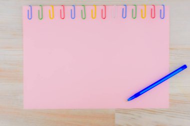 Masanın üzerine renkli ataçlarla tutturulmuş pembe kağıt yaprağı, tükenmez kalemle, arka plan için.