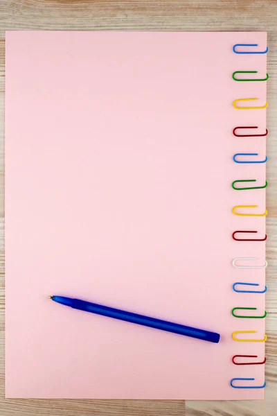 粉红的纸夹在橡木桌上的彩色回形针上 圆珠笔 用来做背景 — 图库照片