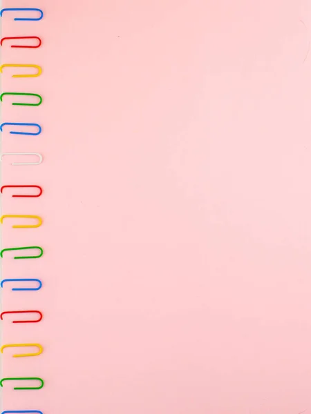 Pink paper sheet fixed with multi-colored paper clips close, for background, vertical