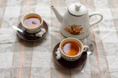 Bir çaydanlık, iki fincan çay, şekerli çay tabakları, kahvaltı masasındaki çay kaşıkları.