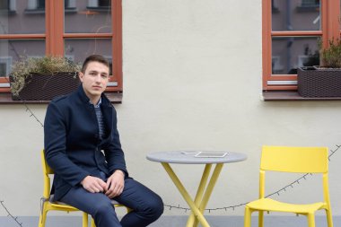 Adam kafenin yakınındaki bir masada oturuyor, masada aletler yatıyor.