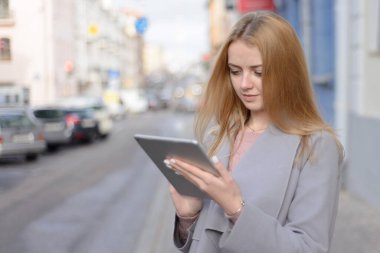 Paltolu kızıl saçlı kız şehir caddesindeki bir tablette bir şeye benziyor.