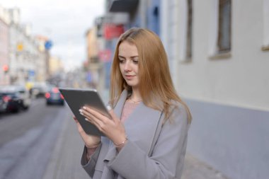 Paltolu kızıl saçlı kız şehir caddesindeki bir tablette bir şeye benziyor.
