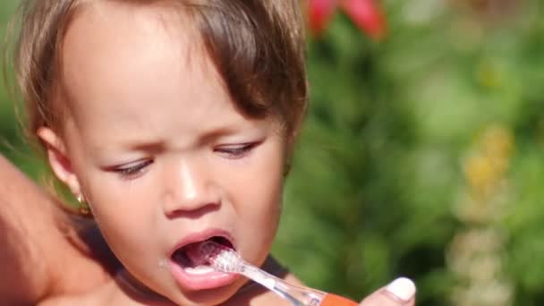 2歳の女の子は夏の庭で歯を磨いています — ストック動画