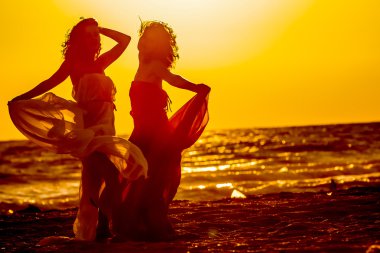 iki genç mutlu kadın, gün batımı deniz arka plan üzerinde siluetleri