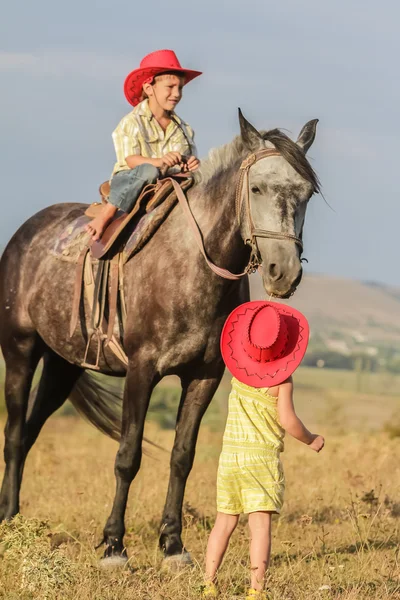 Zwei junge glückliche Kinder auf einem Pferd auf einem Bauernhof, im Freien Portrait auf — Stockfoto