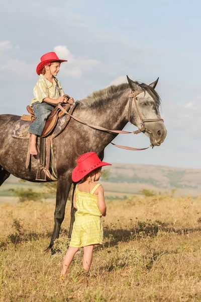 Zwei junge glückliche Kinder auf einem Pferd auf einem Bauernhof, im Freien Portrait auf — Stockfoto