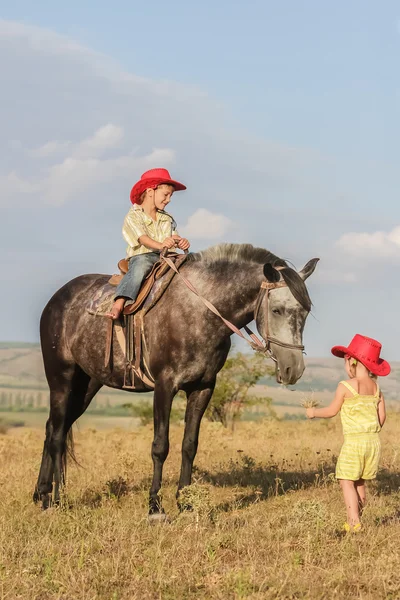 Twee jonge gelukkige jonge geitjes het berijden van een paard op de boerderij, outdoor portret op — Stockfoto