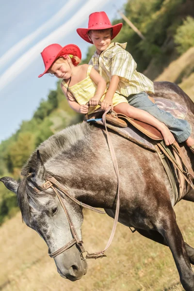 Twee jonge gelukkige jonge geitjes het berijden van een paard op de boerderij, outdoor portret op — Stockfoto