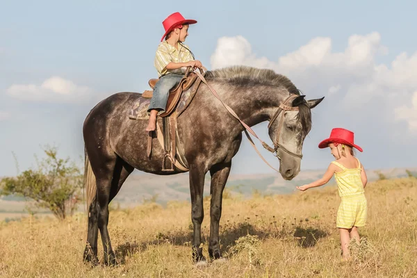 Twee jonge gelukkige jonge geitjes het berijden van een paard op de boerderij, outdoor portret op — Stockfoto