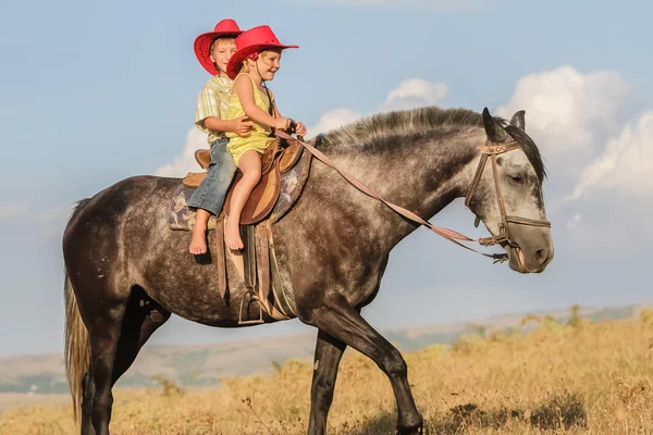 Twee jonge gelukkige jonge geitjes het berijden van een paard op de boerderij, outdoor portret op — Stockfoto