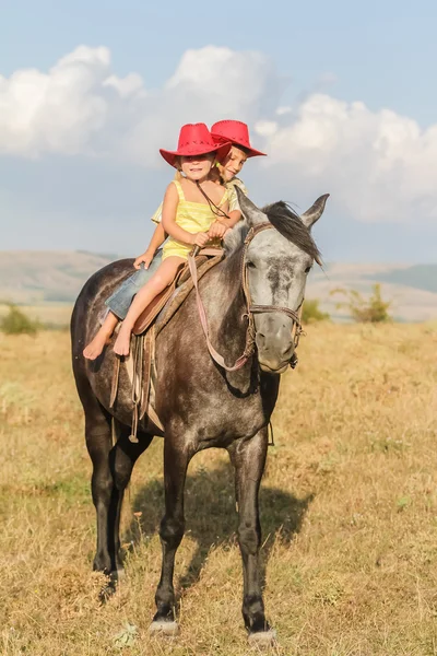 Two young happy kids riding a horse on farm, outdoor portrait on — Stock Photo, Image