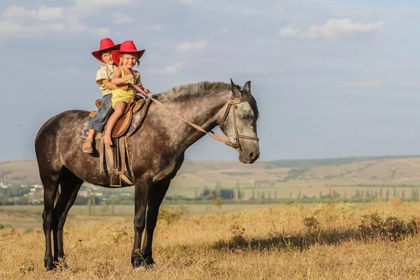 Twee jonge gelukkige jonge geitjes het berijden van een paard op de boerderij, outdoor portret op — Stockfoto