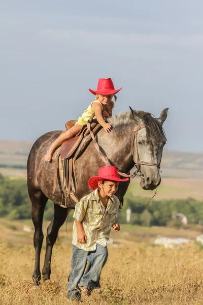Två unga glada barn rida en häst på gården, utomhus porträtt på — Stockfoto