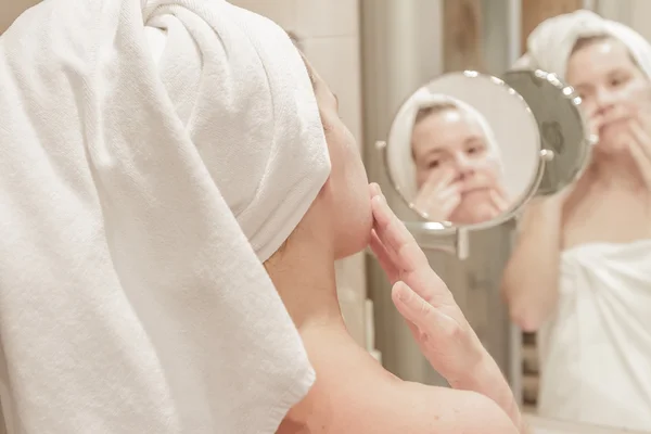 Mulher bonita aplicando creme em seu rosto no banheiro — Fotografia de Stock