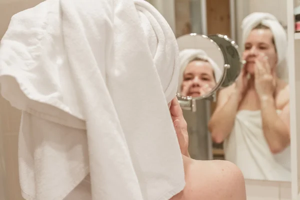 Bella donna che applica la crema sul suo viso in bagno — Foto Stock