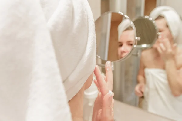 Mulher bonita aplicando creme em seu rosto no banheiro — Fotografia de Stock