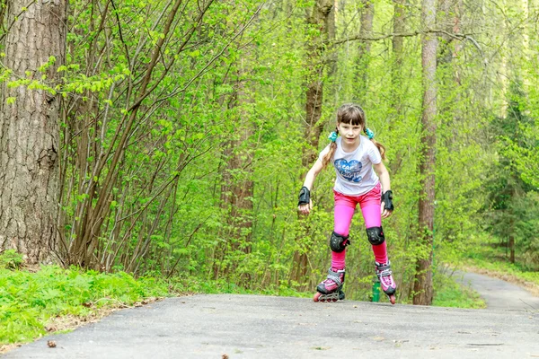 Giovane ragazza in attrezzature protettive e rulli nel parco, all'aperto — Foto Stock