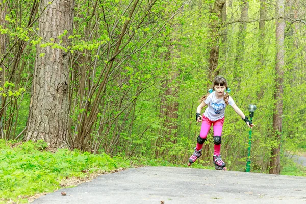 Ung flicka i skyddsutrustning och rullarna i park, utomhus — Stockfoto