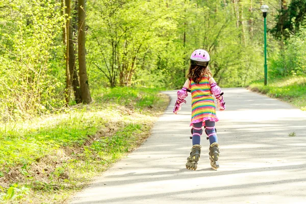 Ung flicka i skyddsutrustning och rullarna i park, utomhus — Stockfoto