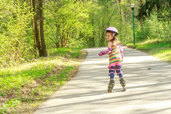 Ung flicka i skyddsutrustning och rullarna i park, utomhus — Stockfoto