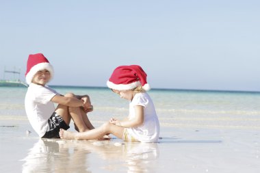 Noel Baba şapkaları tropikal plaj arka plan üzerinde iki genç çocuk