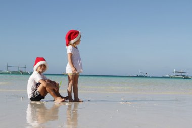 Two young happy children in santa hats on tropical beach backgro clipart