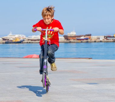 Genç mutlu çocuk faving eğlence doğal zemin üzerine scooter üzerinde