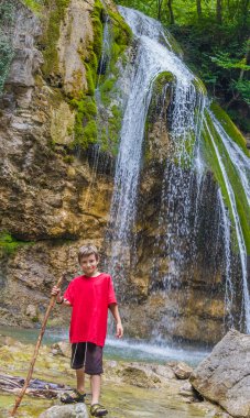 Genç mutlu çocuk boy gülümseyerek şelale arka plan üzerinde