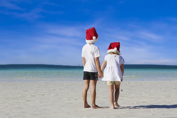 Duas crianças em santa chapéus em fundo de praia tropical — Fotografia de Stock