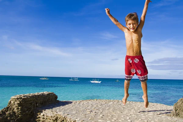 Jong gelukkig kind jongen springen op tropische zee achtergrond — Stockfoto