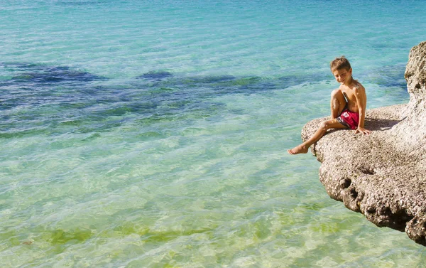 Маленький счастливый мальчик сидит на скалах на тропическом море backgroun — стоковое фото