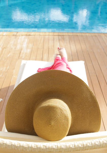 молодая красивая женщина в шляпе отдыхает возле бассейна
