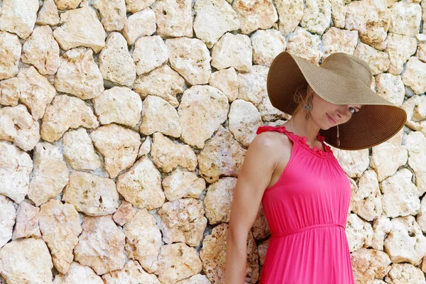 Young beautiful woman in hat standing next to stone wall — Stock Photo, Image