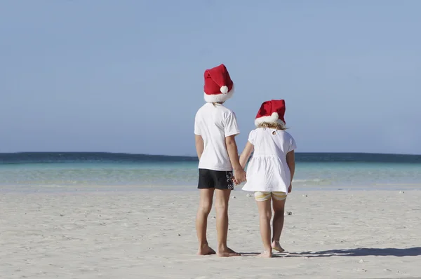 Dos niños pequeños en sombreros de santa sobre fondo de playa tropical —  Fotos de Stock