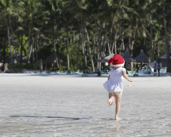 Criança em santa hat correndo pela praia tropical — Fotografia de Stock